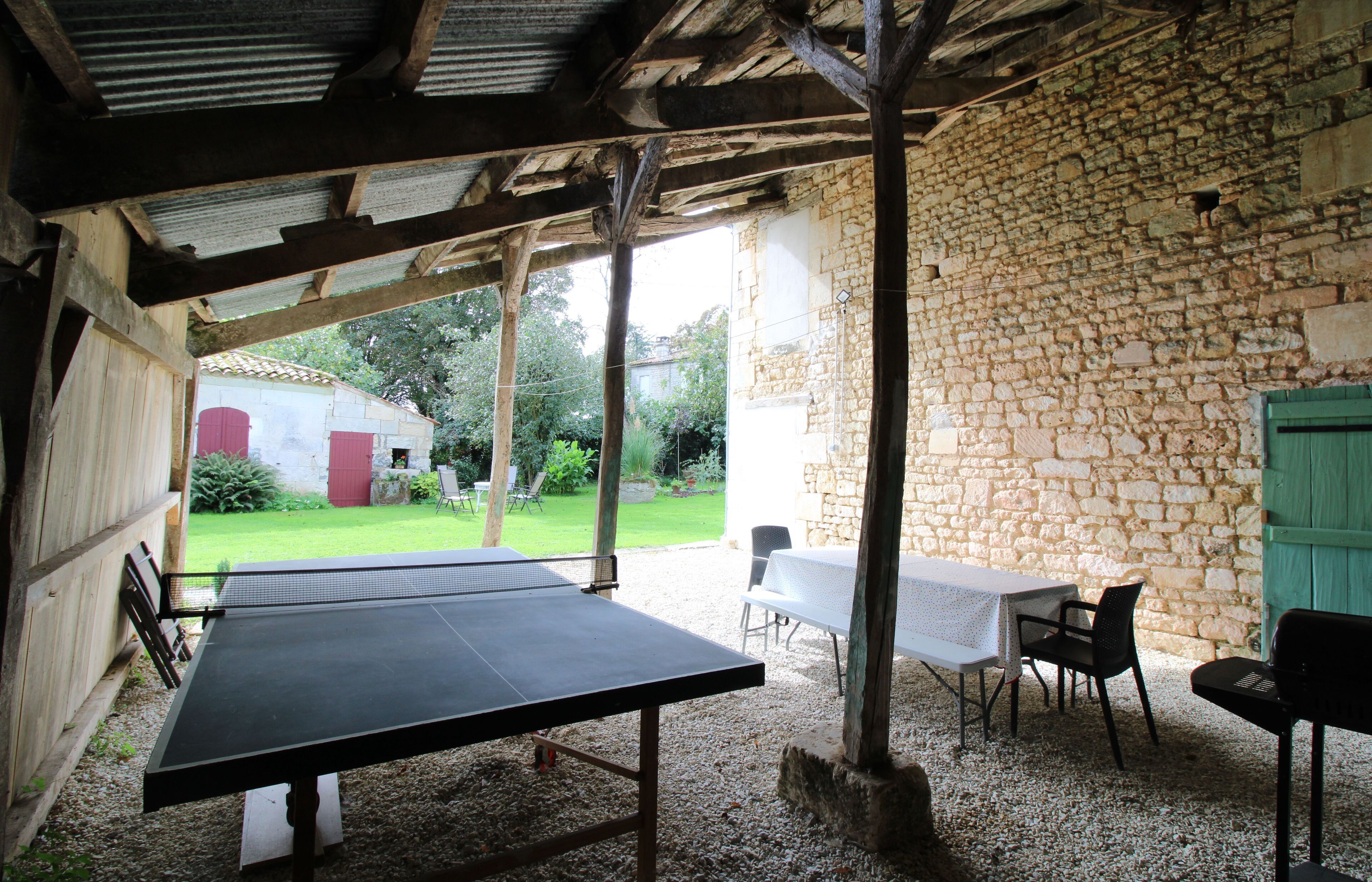 Un espace extérieur comprenant une table de ping-pong, des murs en pierre et un coin salon couvert avec des tables et des chaises.