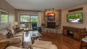 Una sala de estar con chimenea de piedra, televisor montado en la pared y balcón con vista a la ciudad.