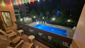 A balcony with a swimming pool, lounge chairs, and a small building.