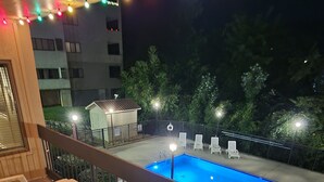 Un balcón con piscina, sillas de descanso y luces colgantes.