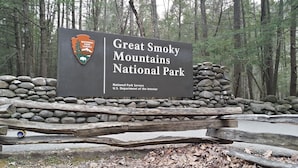 Señal de Great Smoky Mountains National Park con un muro de piedra y una valla de madera al frente.