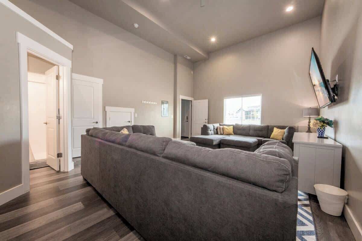 Un salón amplio con un sofá seccional gris grande, un sofá gris pequeño y un mueble blanco.