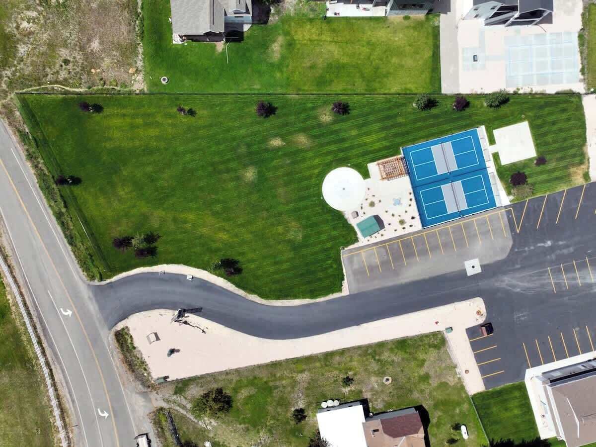 An aerial view of a property with a curved road, a parking lot, a tennis court, and a building with a dome-shaped structure.