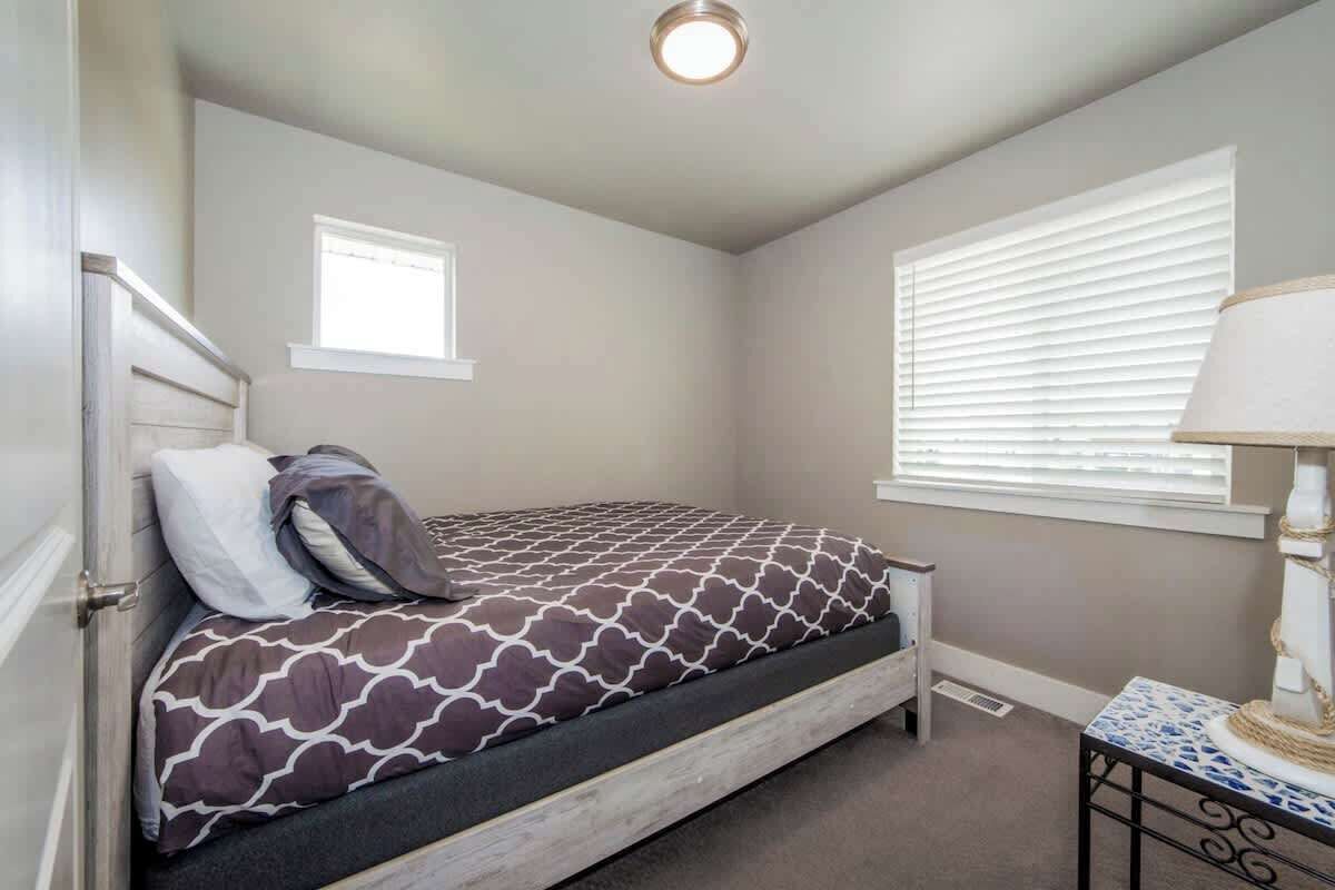 Un dormitorio con cama, ventana con persianas, mesita de noche y lámpara.