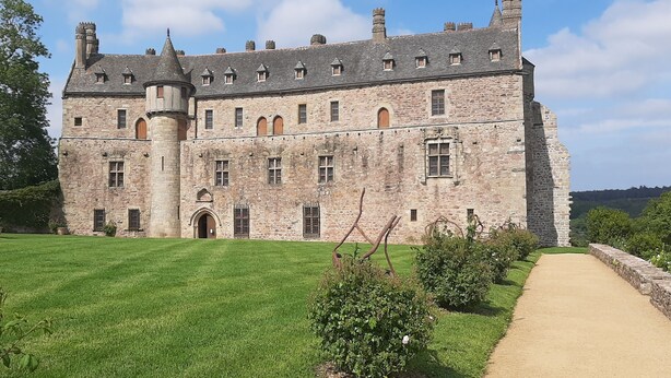 Un gran castillo de piedra con una torre central, rodeado de un césped y jardín bien cuidados.