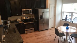 A kitchen with dark cabinets, stainless steel appliances, a granite countertop, and a dining area with a round table and chairs. - Stylish townhome- Close to the glorious Rehoboth Beaches (Rehoboth Beach)