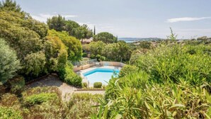 A pool surrounded by lush greenery and a view of the sea.