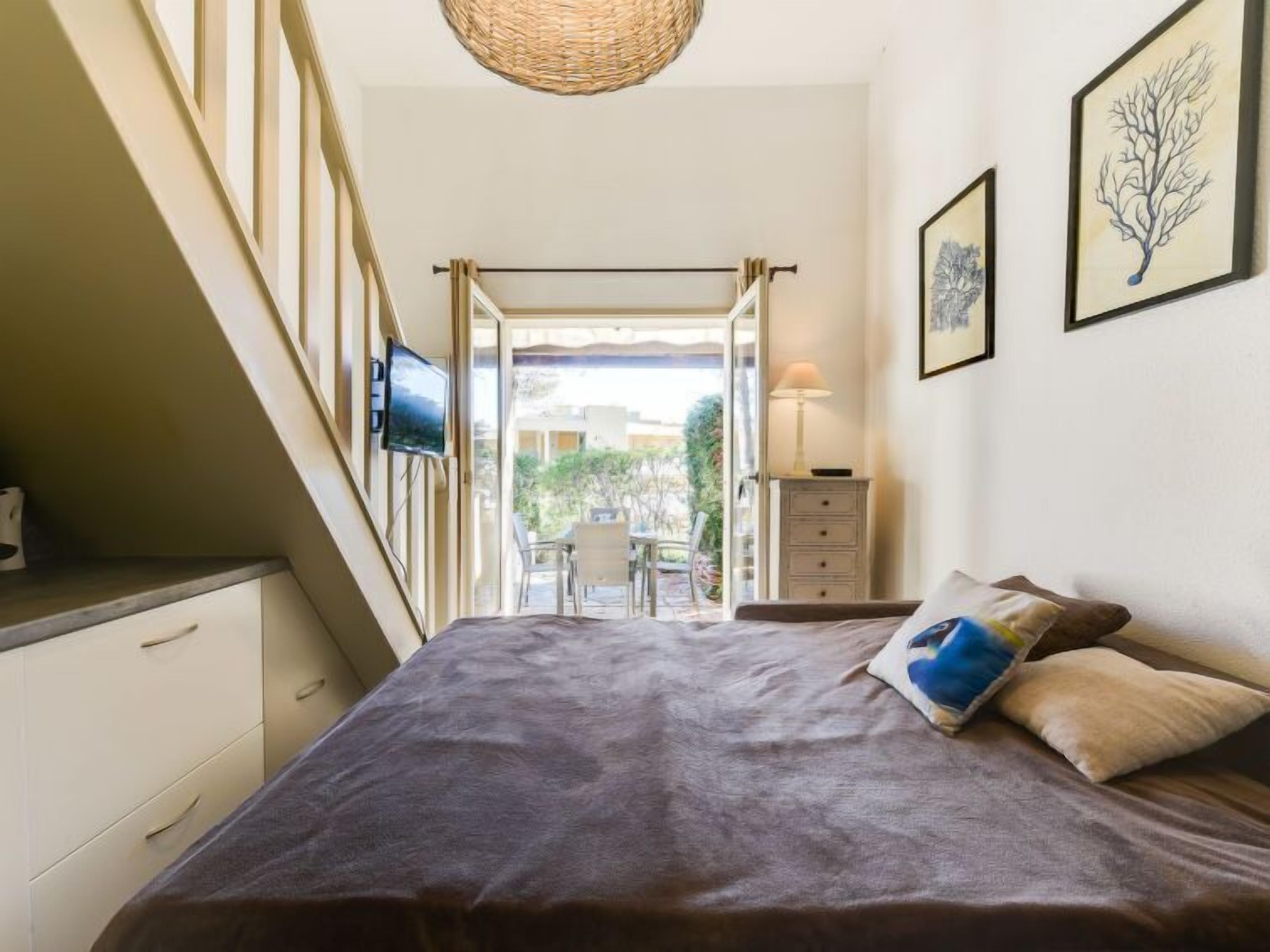 Ein Schlafzimmer mit Bett, Fernseher, Kommode und Blick ins Freie.