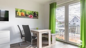 Una habitación moderna con una mesa de comedor, sillas, un televisor de pantalla plana y un cuadro con velas y flores.