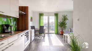 Una cocina moderna con comedor, un balcón con cortinas verdes y una planta en maceta.
