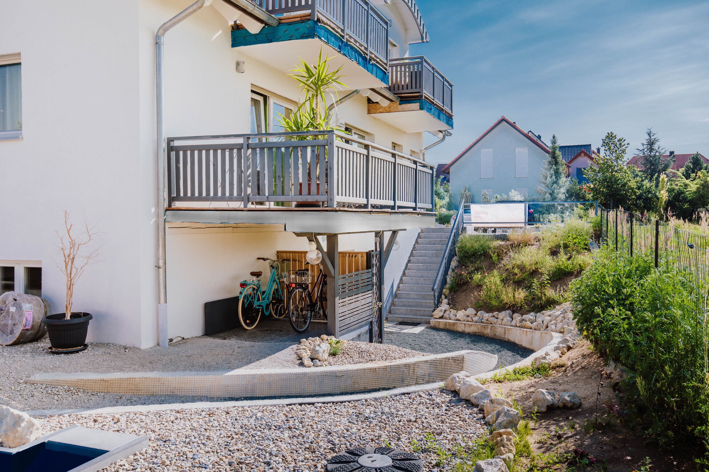 Ein mehrgeschossiges Wohngebäude mit Balkon, einem kleinen Garten mit Pool und abgestellten Fahrrädern.
