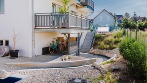Un edificio residencial de varios pisos con un balcón, un pequeño jardín con piscina y bicicletas estacionadas afuera.