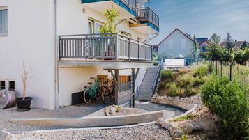 Ein mehrgeschossiges Wohngebäude mit Balkon, einem kleinen Garten mit Pool und abgestellten Fahrrädern.