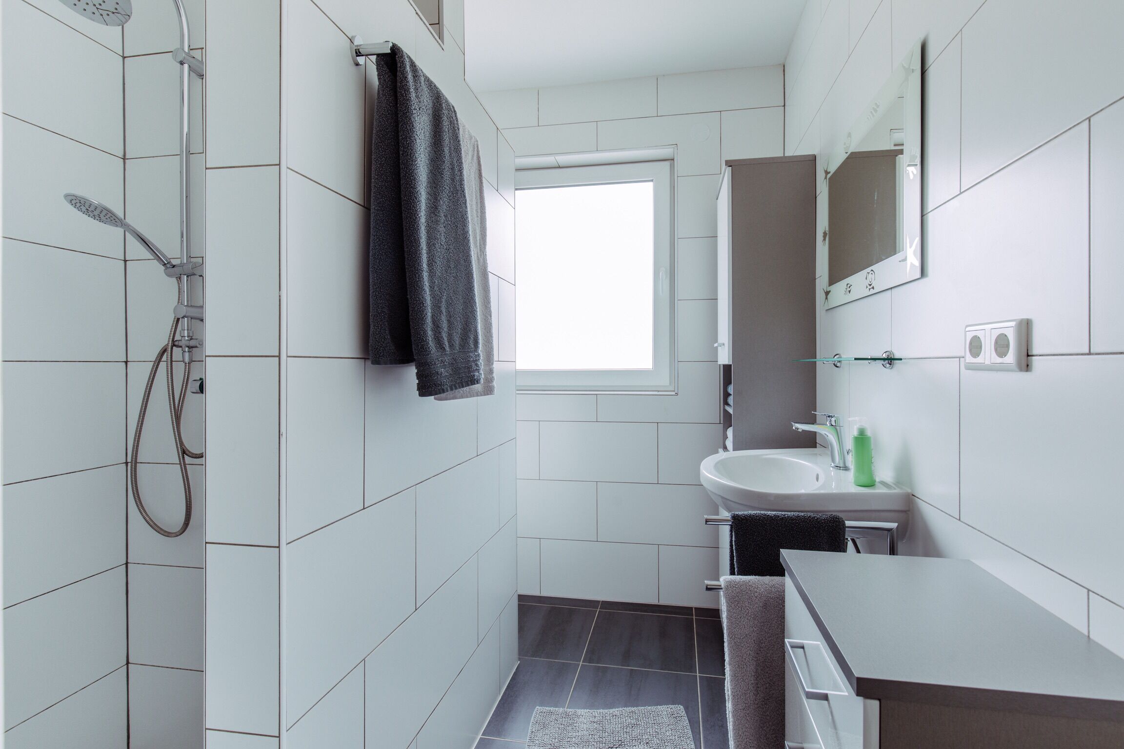 A modern bathroom with white tiles, a shower, a sink, and a mirror.