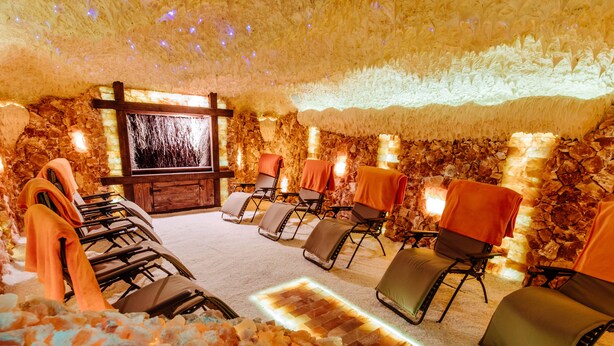 Un cuarto de spa con paredes de piedra, una pantalla grande y varias sillas de masaje.