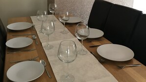 Ein Esstisch, gedeckt mit weißen Tellern, Besteck und Weingläsern, mit einem Tischläufer mit Muster.
