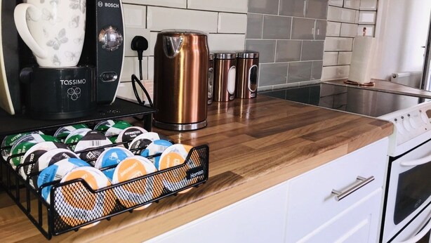 Eine Küche mit Kaffeemaschine, Wasserkocher und einer weiteren Kaffeemaschine. Auf der Arbeitsfläche stehen Tassen und eine Kapselhalterung mit Kaffeekapseln.