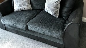 Ein dunkelgraues Sofa mit zwei passenden Kissen, platziert vor einer schlichten Wand mit einer Metallwanddekoration darüber.