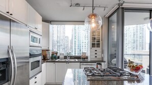 A modern kitchen with stainless steel appliances, a granite countertop, and a city view through large windows.