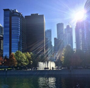 A cityscape with modern high-rise buildings, a body of water, and a fountain in the foreground. - Luxury Coal Harbour 2 bed 2 bath w/ Stunning Views (Vancouver)