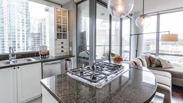 A modern kitchen with a gas stove, granite countertops, and a large window overlooking a cityscape.