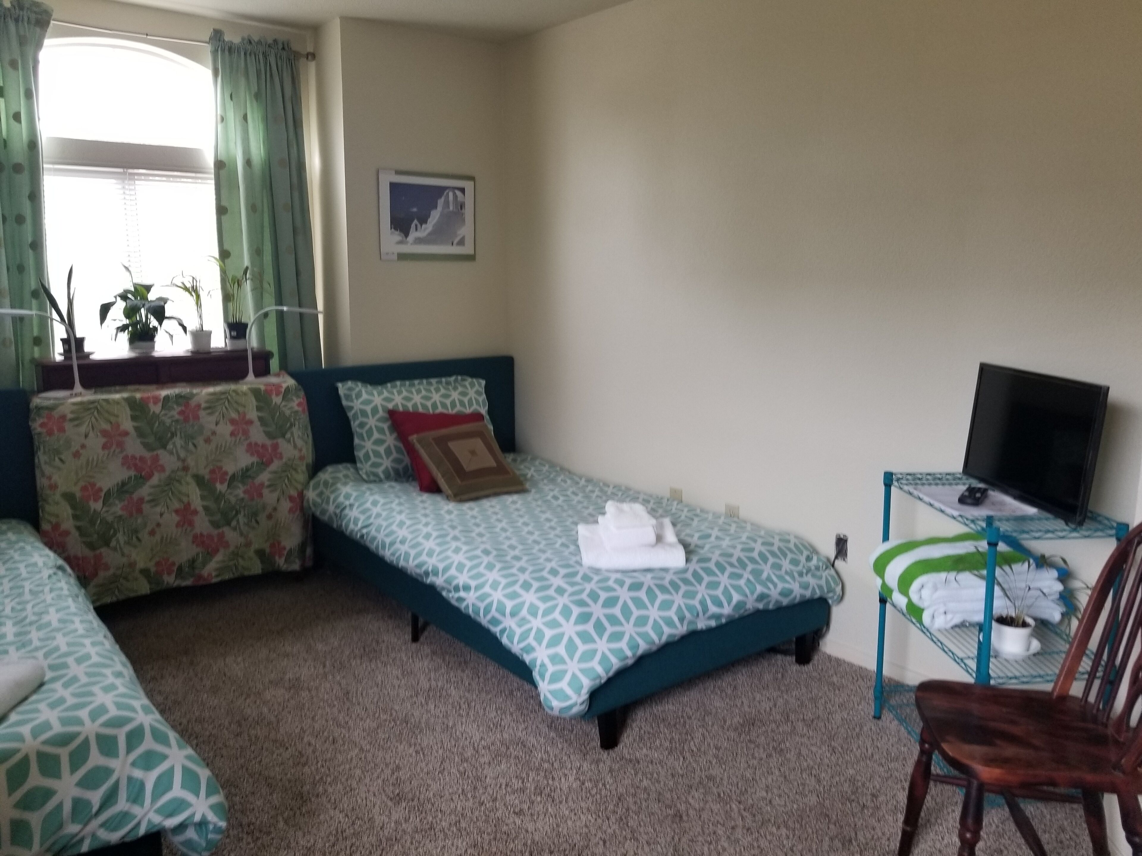 A bedroom with two beds, a desk with a TV, and a chair.