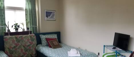 A bedroom with two beds, a desk with a TV, and a chair.
