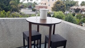 Ein runder Tisch mit zwei Korbstühlen und zwei Weingläsern auf einem Balkon mit Blick auf eine Wohngegend.