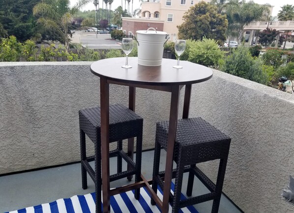 A round table with two wicker chairs and two wine glasses on a balcony with a view of a residential area.