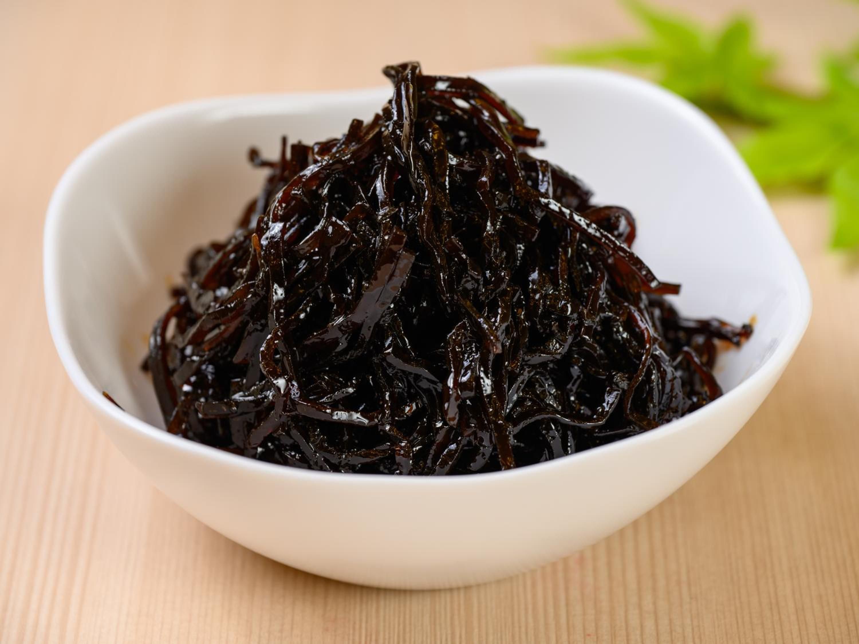 A white bowl filled with dark-colored seaweed on a wooden surface.