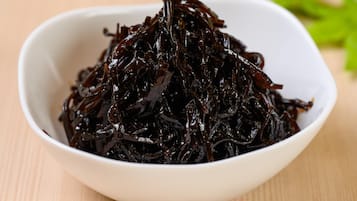 A white bowl filled with dark-colored seaweed on a wooden surface.