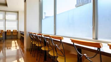 A row of wooden chairs with metal frames, arranged in a line along a window with a view of a building outside.