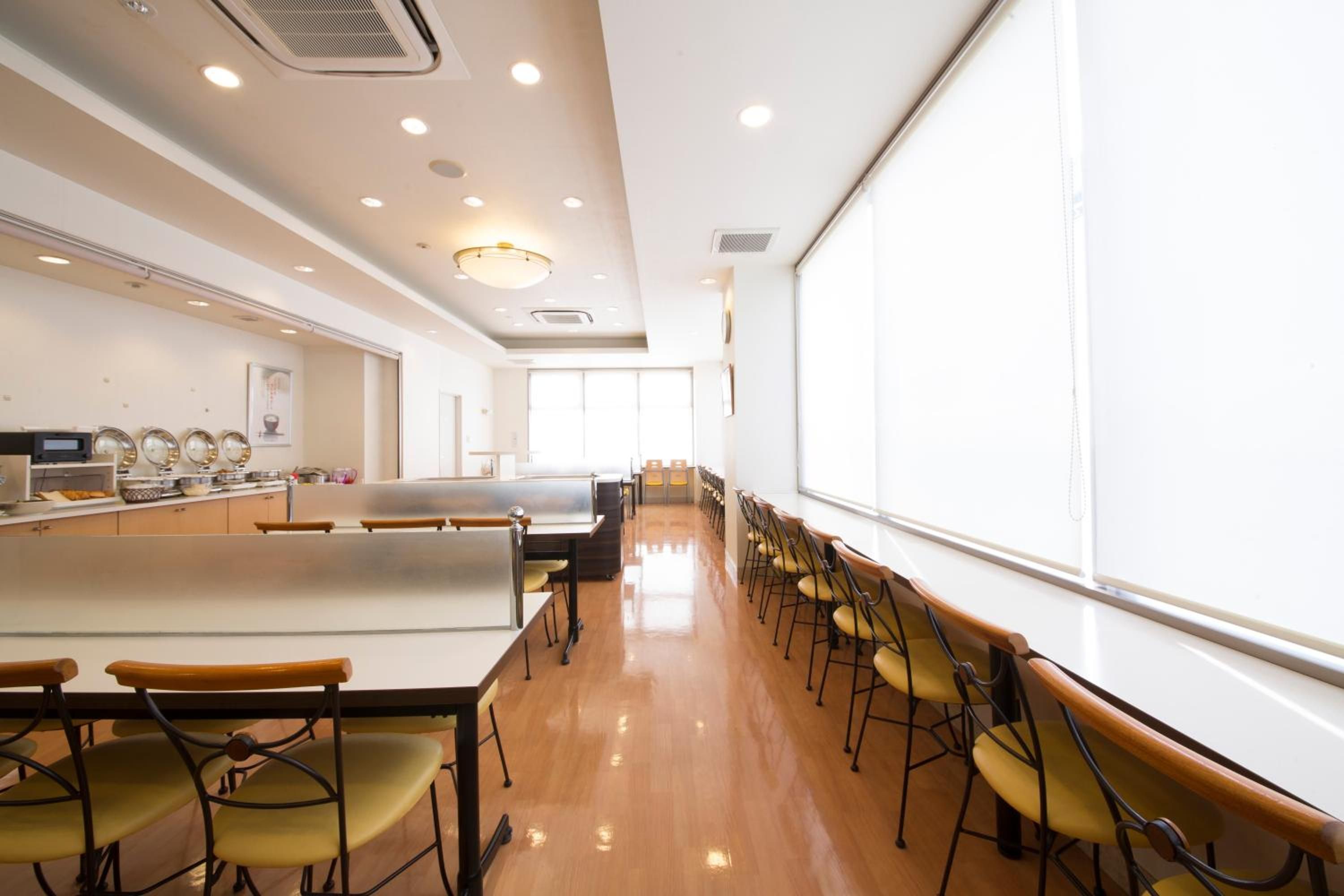 A conference room with a long table, chairs, a projector screen, and a kitchen area with appliances.