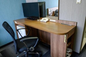 Une chambre d’hôtel avec un bureau en bois, un fauteuil de bureau noir, un écran d’ordinateur, un téléphone et un miroir.