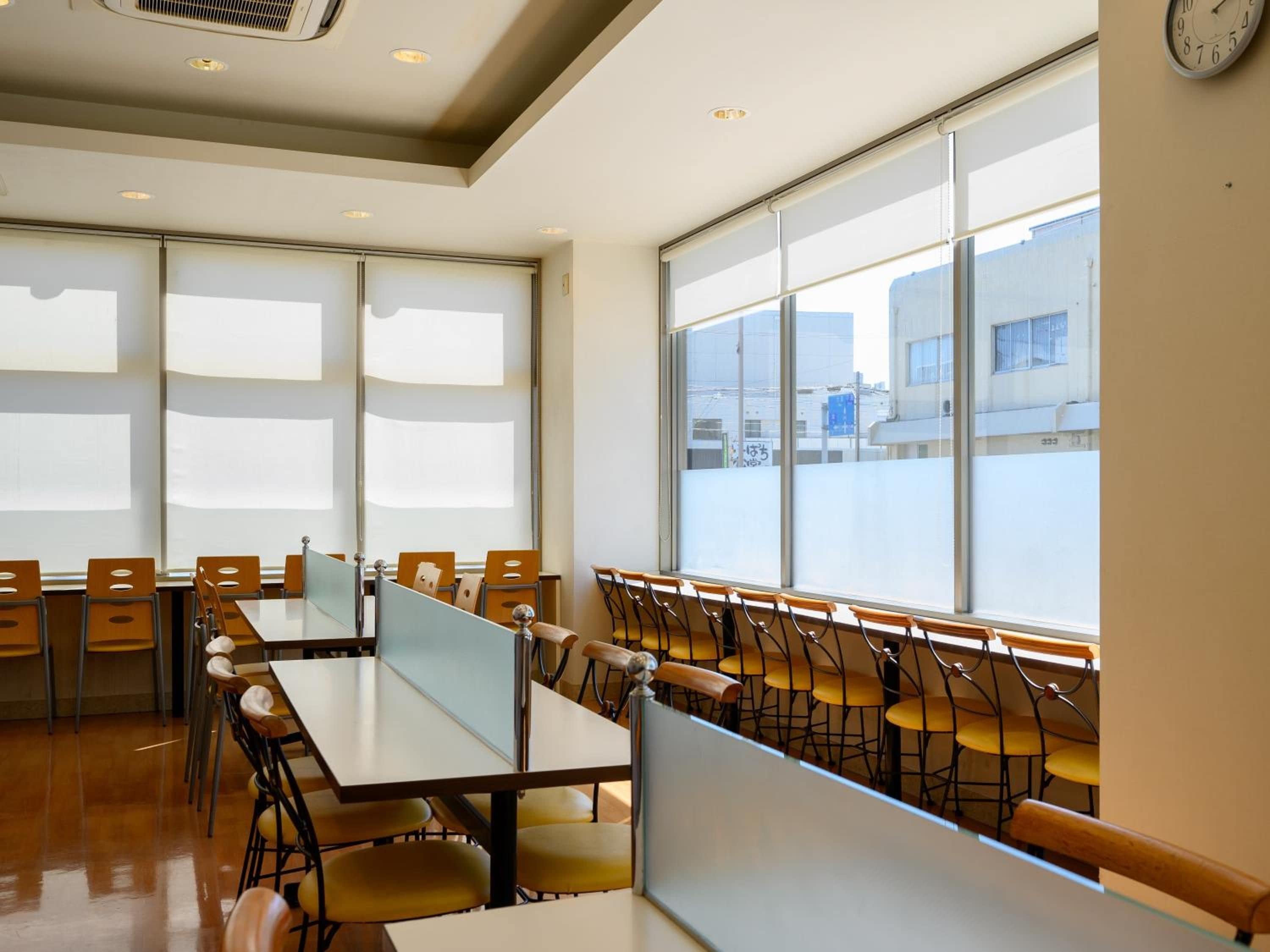 A conference room with tables and chairs, large windows, and a clock on the wall.