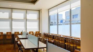 A conference room with tables and chairs, large windows, and a clock on the wall.