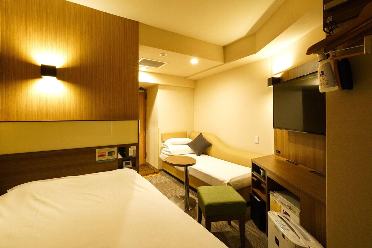 Una habitación de hotel con una cama grande, una cama más pequeña, un escritorio con una silla, un televisor y un minibar.
