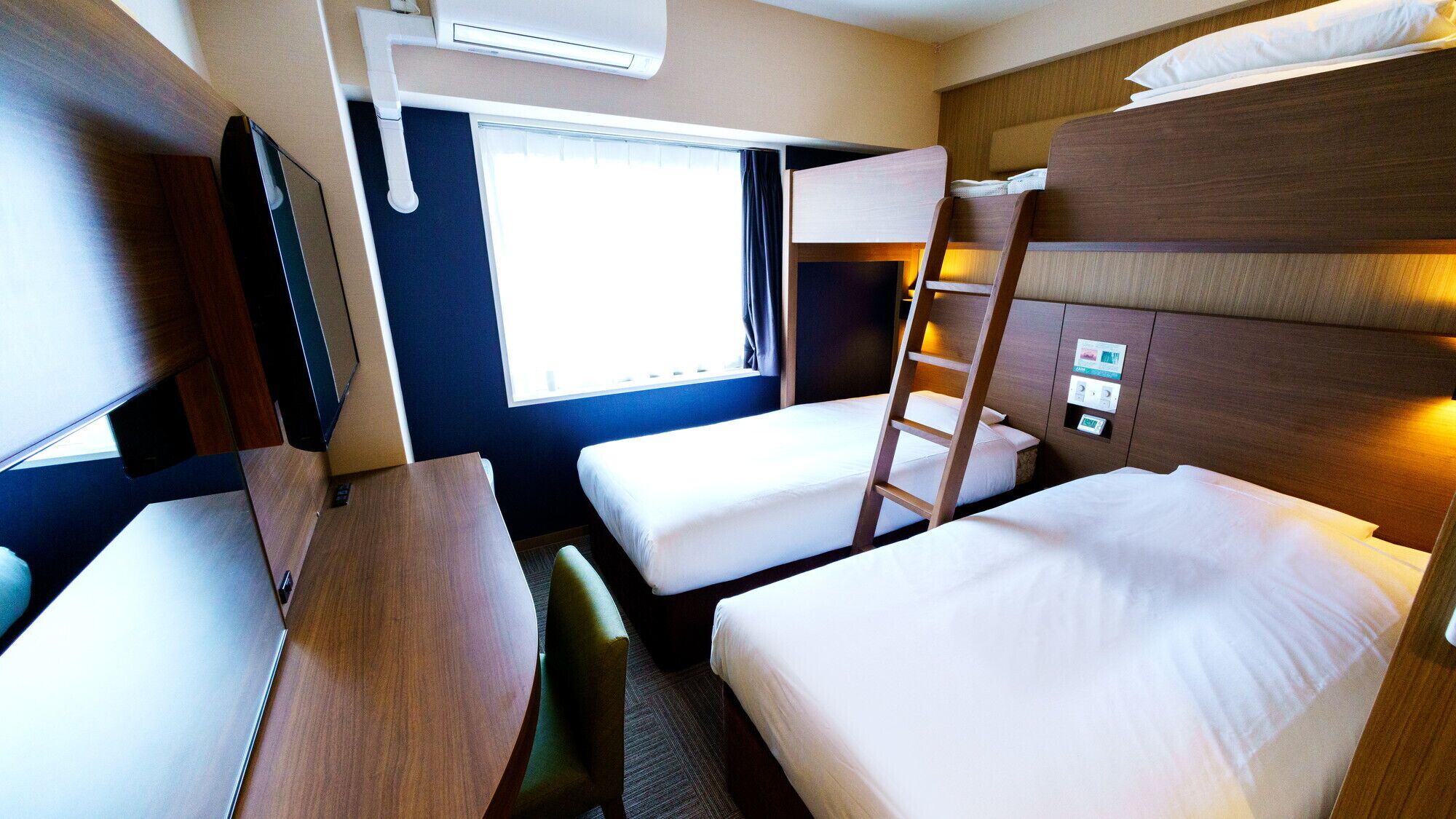 A compact, well-lit room with bunk beds, a desk, and a window providing natural light.