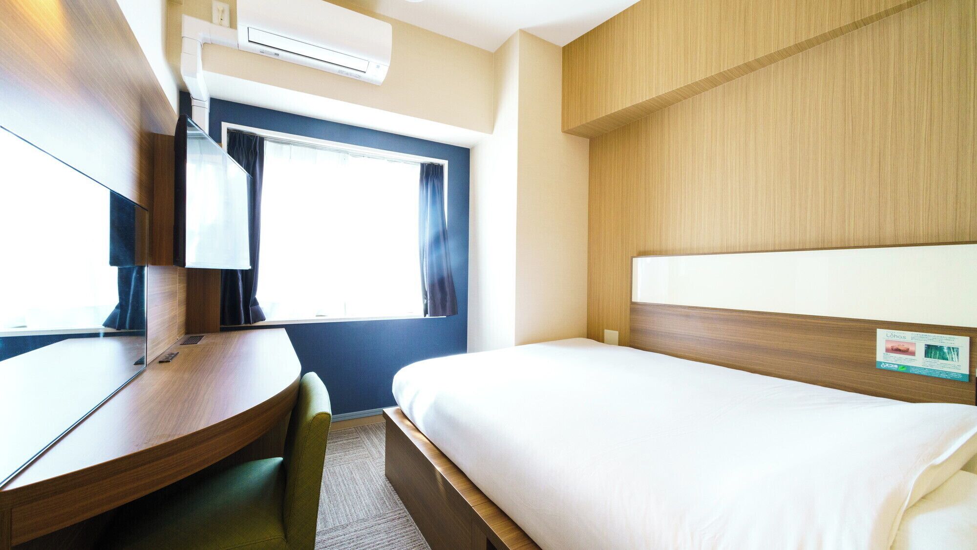 Une chambre d’hôtel équipée d’un lit, d’un bureau, d’une chaise, d’une fenêtre avec des rideaux et d’un appareil de climatisation.