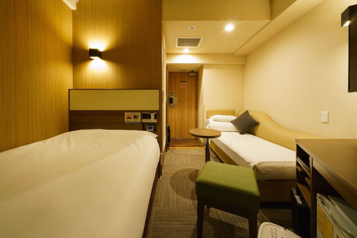 Ein Hotelzimmer mit zwei Betten, einem kleinen Tisch, einer Bank und einem Schreibtisch.