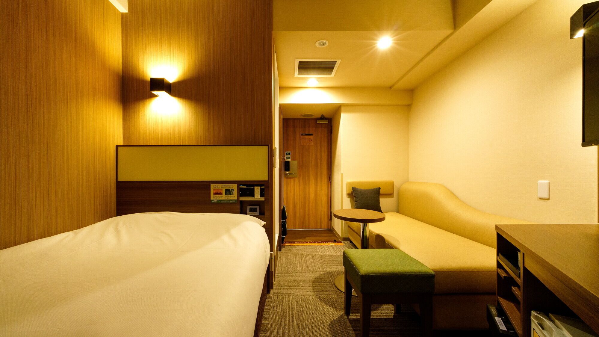 A hotel room with a bed, a sofa, a small table, and a TV.