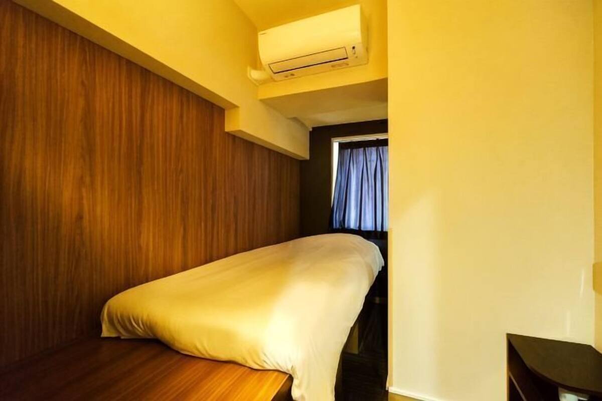 Una habitación pequeña y compacta con una cama individual, una pared de madera y una ventana con cortinas.