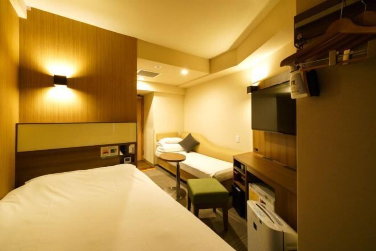 Habitación de hotel con una cama grande, un escritorio pequeño, una silla, una mesita de noche, una lámpara y un televisor.
