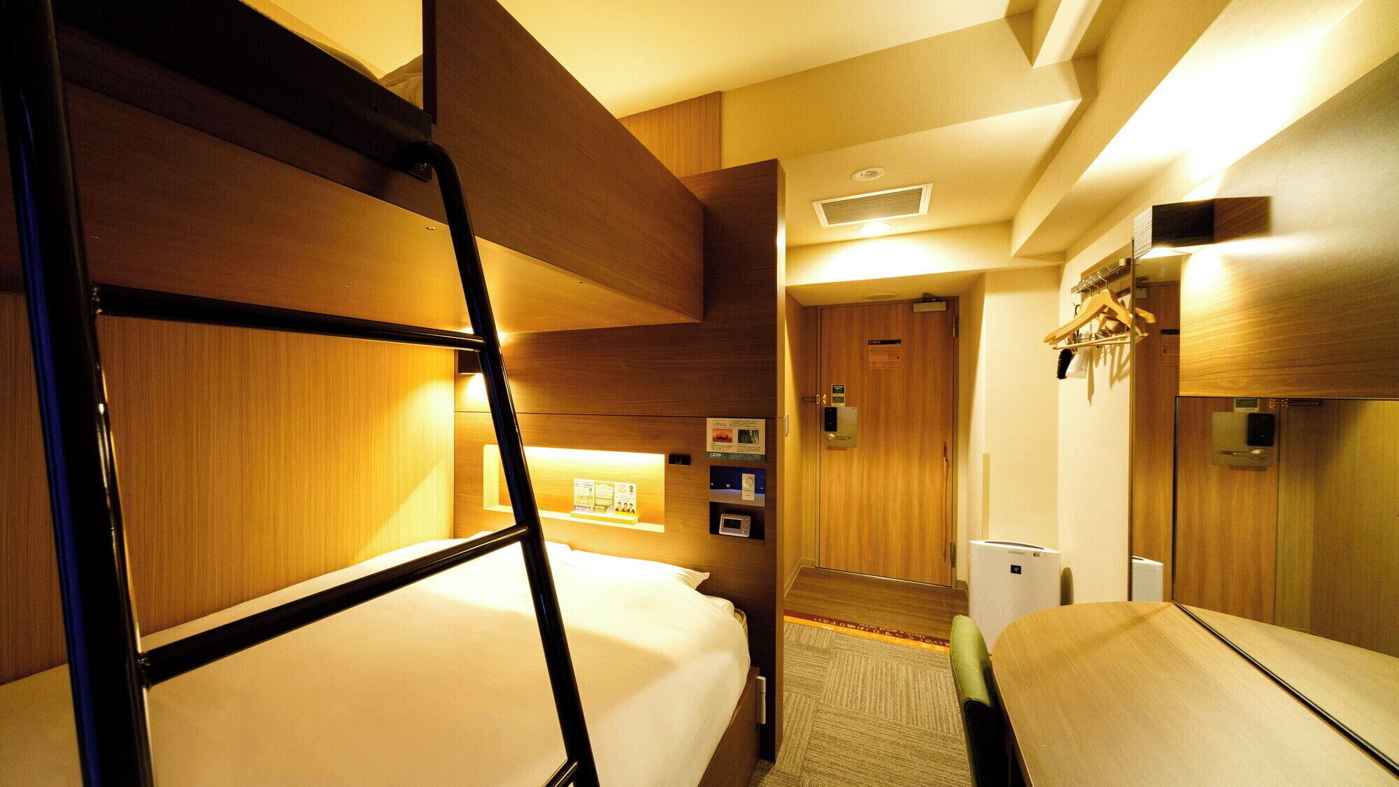 Une chambre d’hôtel avec des lits superposés, un bureau, un four à micro-ondes et un petit coin salon.