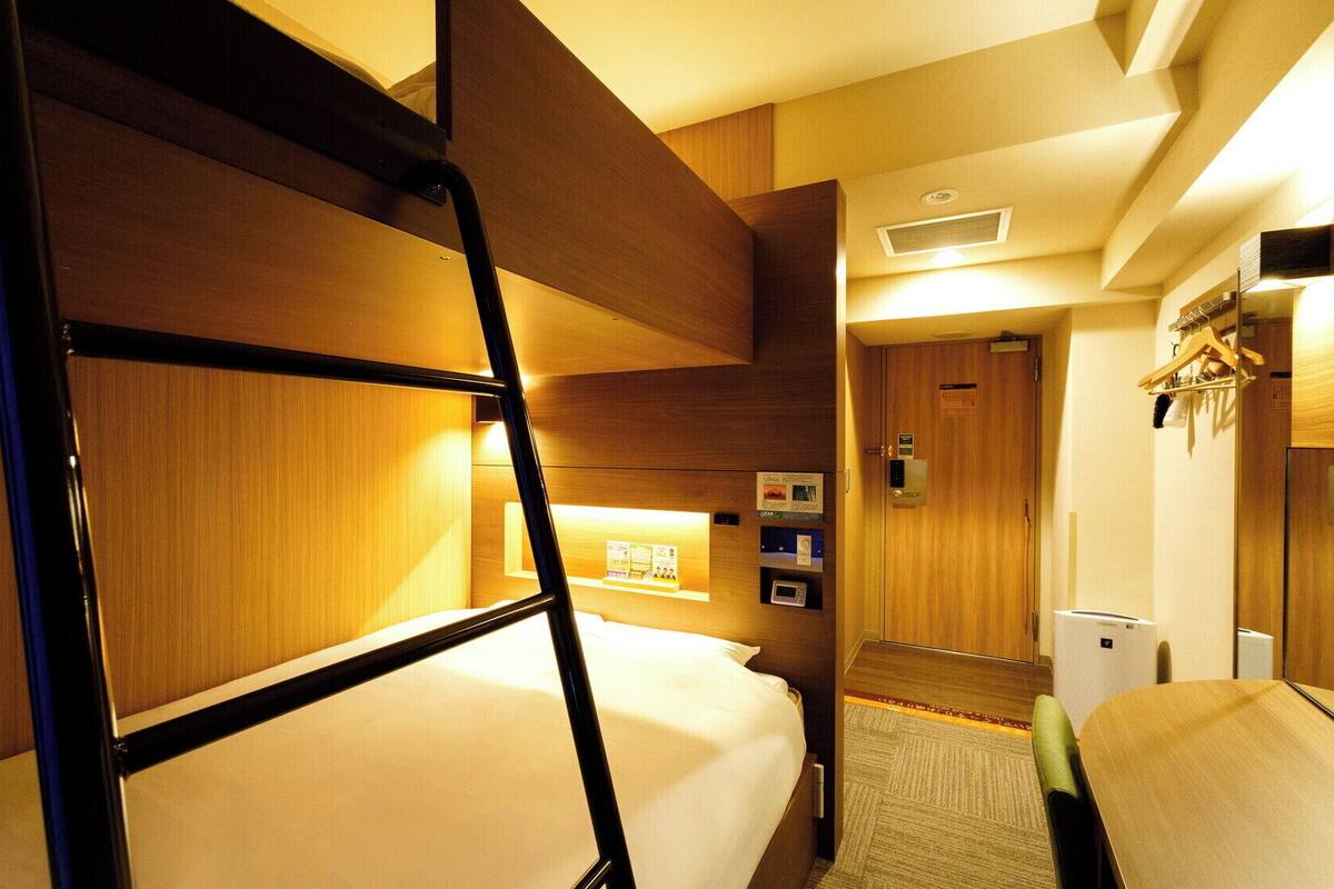 Habitación de hotel con literas, escritorio, microondas y un pequeño rincón de descanso.