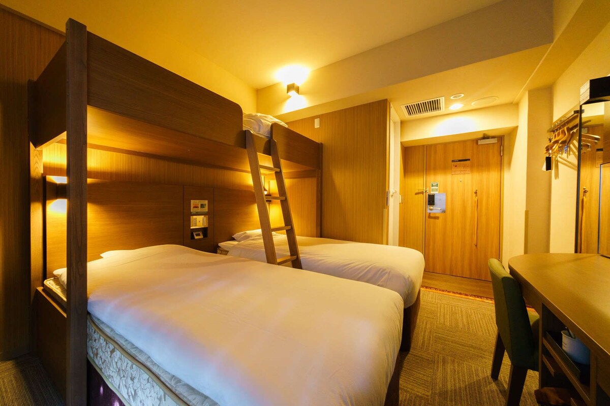 A hotel room with two beds, a desk, a chair, and a wardrobe.