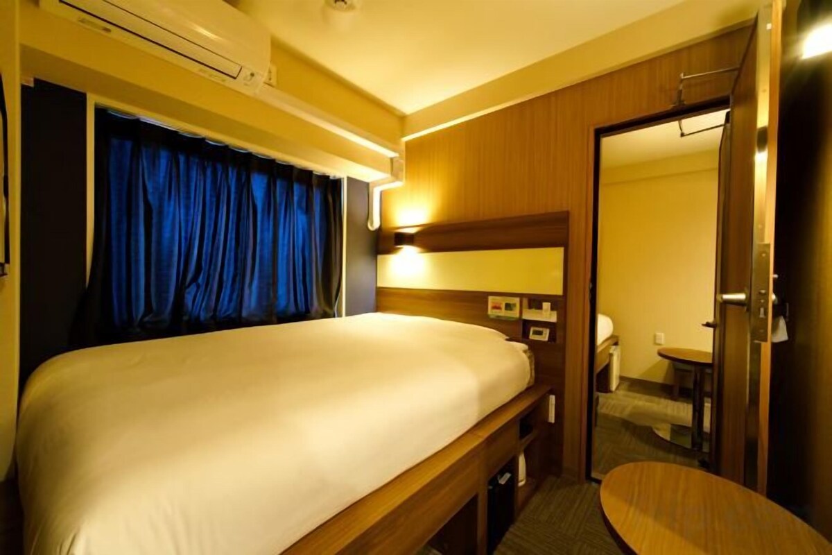 A hotel room with a bed, a desk, a chair, a bathroom, and a door.