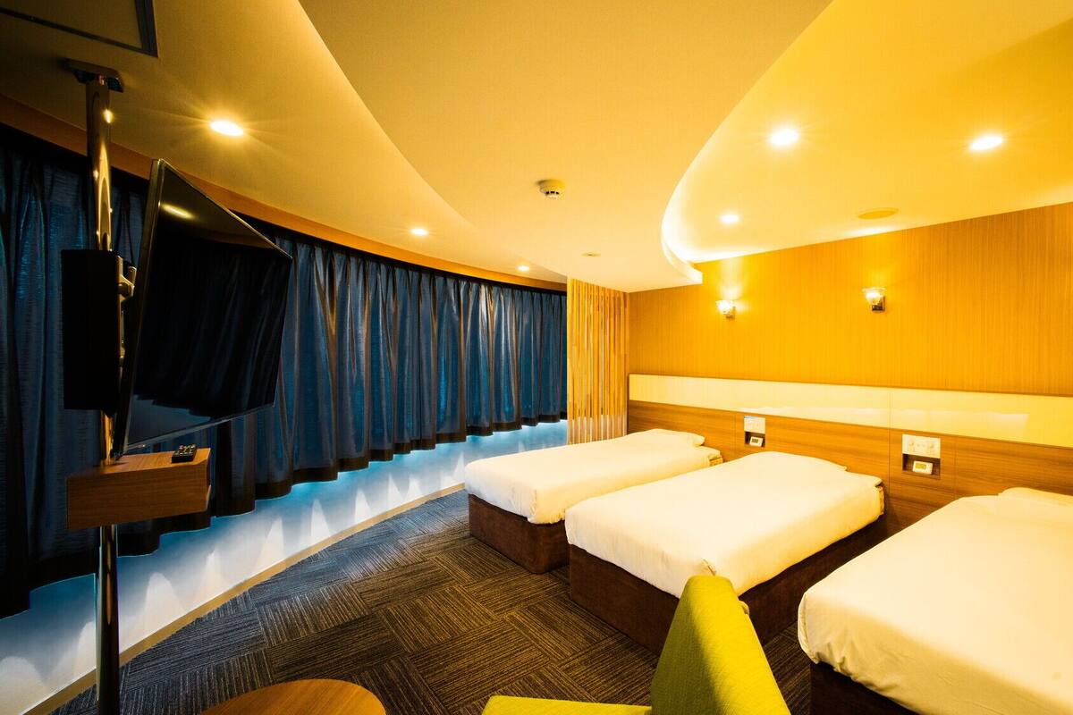 Habitación de hotel con techo curvo, tres camas, un televisor y una escalera.