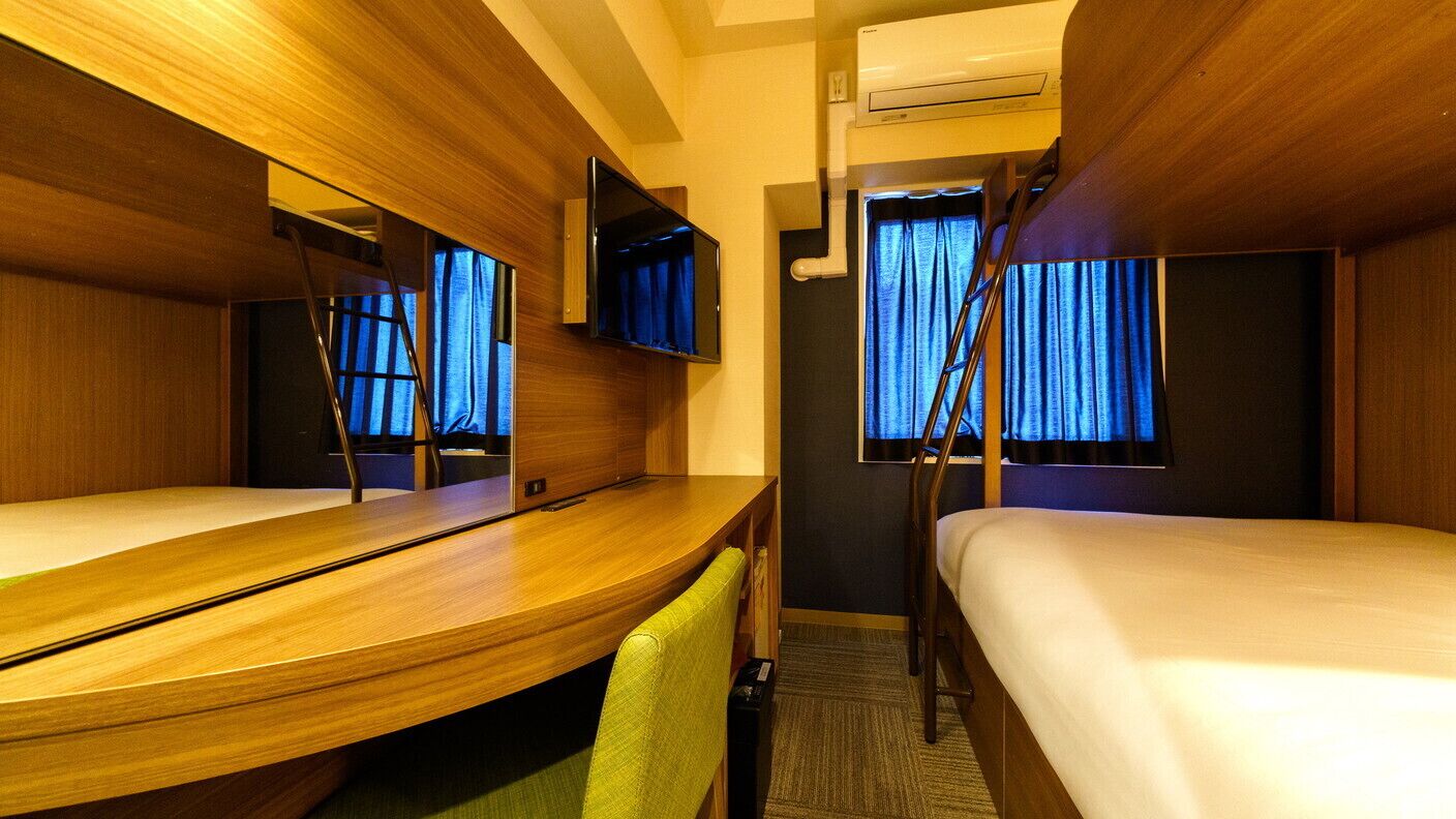 A hotel room with a bed, a desk, a chair, a TV, and a window with curtains.