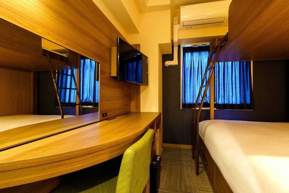 Habitación de hotel con cama, escritorio, silla, televisor y ventana con cortinas.